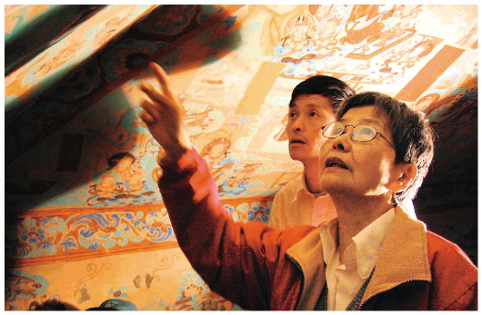 ▲樊錦詩（右一）在莫高窟第八十五窟壁畫修復現(xiàn)場。（敦煌研究院供圖）